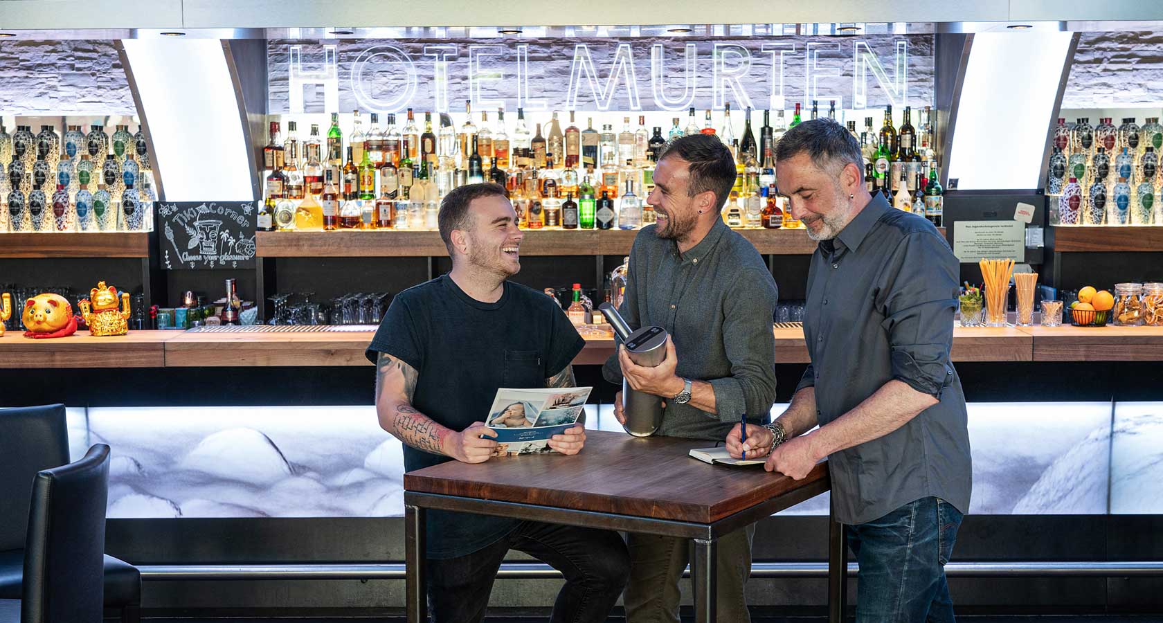 3 Männer stehen an einem Bar-Tisch.