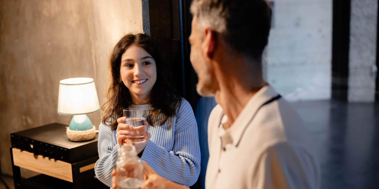 A man and a woman sit relaxed in the living room and drink fresh water together.