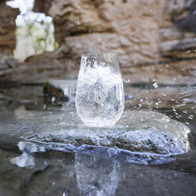 A glass of water stands on a stone outside.