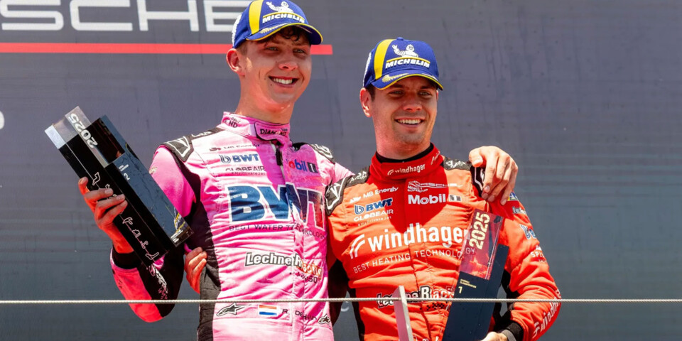 Two professional race car drivers stand on the podium celebrating victory at a Porsche motorsport event.